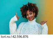 ctp afroamerican young woman in white sweater with thumbs up while pointing to right. Стоковое AI-изображение, AI-художник Юлия Гапеенко / Фотобанк Лори
