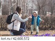 A handsome, cheerful little boy of two years old walks with his mother on the street in the spring. The kid plays and collects flowers for his mother in the park. The concept of parenthood, childhood and family. Стоковое фото, фотограф Photojuli / Фотобанк Лори