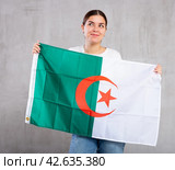Joyous young woman holding Algeria flag against unicoloured background. Стоковое фото, фотограф Яков Филимонов / Фотобанк Лори