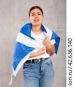 Sad young woman holding Scotland flag against unicoloured background. Стоковое фото, фотограф Яков Филимонов / Фотобанк Лори