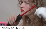 The woman with the beautiful long blonde hair is using a curling wand to style her hair. She's recording a vlog on phone while manually wrapping hair around the wand (2024 год). Редакционное видео, видеограф А. А. Пирагис / Фотобанк Лори
