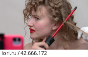 A young woman with long hair is using a curling wand to style hair, manually wraps sections of blonde hair around the wand. Broadcast live video to social media (2024 год). Редакционное видео, видеограф А. А. Пирагис / Фотобанк Лори