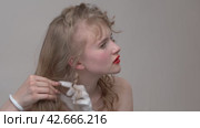 Close-up view of a Caucasian young woman carefully and expertly untangling her long hair as she grooms herself in a hairdressing salon, creating a stunning new look (2024 год). Редакционное видео, видеограф А. А. Пирагис / Фотобанк Лори