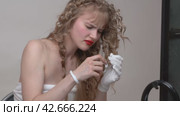 The blondie young woman impatiently removed her hair elastic and untangled her blonde long hair while having it curled during hair care at a beauty salon (2024 год). Редакционное видео, видеограф А. А. Пирагис / Фотобанк Лори