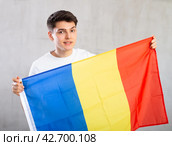 Happy young man holding flag of Romania against unicoloured background. Стоковое фото, фотограф Яков Филимонов / Фотобанк Лори