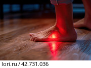 Barefoot walking on dark wooden floor. Bare foots with red effect of pain. Painful gout inflammation. Tingling and burning sensation in foot. Sensory neuropathy problems. Healthcare and podiatry. Legs. Стоковое AI-изображение, AI-художник Марина Демидюк / Фотобанк Лори