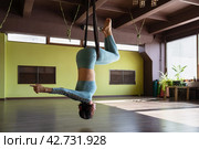A woman performs an asana in a hammock with an inverted body position, hanging upside down, working out in sportswear, concept on the theme of aerial yoga. Стоковое фото, фотограф Сергей Чайко / Фотобанк Лори