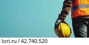 A construction worker stands sideways in a yellow protective vest and holds a helmet in his hands. Copy space. Стоковое AI-изображение, AI-художник Ярославский Максим / Фотобанк Лори