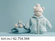Stack of baby knitted clothes and teddy bear toy on table. Set of newborn child rompers, hat and jumper. Fashion infant accessories isolated pastel blue background, empty space. Kid's toys and clothes. Стоковое AI-изображение, AI-художник Марина Демидюк / Фотобанк Лори