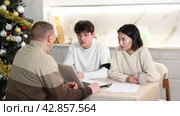 Male realtor discusses the terms of contract with couple in office of real estate agency, offering various accommodation options against backdrop of a Christmas tree. Стоковое видео, видеограф Яков Филимонов / Фотобанк Лори