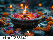 Burning bowl decorated with colorful flower petals that float in the water around it. The bowl is made of stone with a carved pattern around the edge. The fire in the bowl is bright and vigorous, its flames creating a cozy glow reflected on the water surface. All this creates an atmosphere of meditativeness and calm. The scene's components are set against a backdrop of rocks and water, adding elements of nature and harmony. Стоковое AI-изображение, AI-художник Анна Кривицкая / Фотобанк Лори