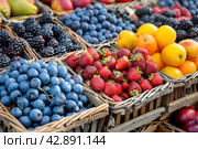 A variety of fresh fruit in overflowing baskets on the counter. Стоковое AI-изображение, AI-художник Юрий Поздников / Фотобанк Лори