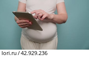 Pregnant woman holding digital tablet Apple iPad, studio blue background. Pregnancy and modern technology concept - Moscow, Russia, April 19, 2024. Редакционное видео, видеограф Андрей Журавлев / Фотобанк Лори