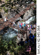ARSHAN VILLAGE, TUNKINSKIY DISTRICT, BURYATIA, RUSSIA -  August 12, 2023: People on suspension bridge admire beautiful waterfall on mountain river Kyngarga - natural attraction in Tunkinskiy Park reserve. Редакционное фото, фотограф Виктория Катьянова / Фотобанк Лори