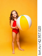 Happy little girl wearing red swimsuit holding beachball on yellow background. Summer vacation and childhood concept. Active lifestyle. Стоковое фото, фотограф Ирина Михайличенко / Фотобанк Лори