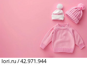 Stack of baby knitted clothes on a table. Set of newborn child rompers, hat and jumper. Fashion infant accessories isolated pastel pink background, empty space. Kid's toys and clothes. Стоковое AI-изображение, AI-художник Марина Демидюк / Фотобанк Лори
