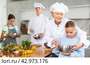 During childrens cooking class, female chef helps girl thoroughly stir homogeneous dough with whisk. Стоковое фото, фотограф Яков Филимонов / Фотобанк Лори