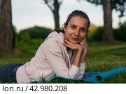 Portrait of dreamful woman lying on yoga mat on the grass. Стоковое фото, фотограф Константин Григорьев / Фотобанк Лори