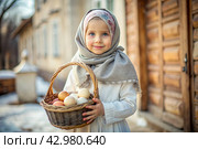 Happy bright Easter. Christianity. Portrait of a three-year-old girl in a Russian folk dress and shawl with a wicker basket with Easter eggs in her hands against the background of an Orthodox church. Стоковое AI-изображение, AI-художник Photojuli / Фотобанк Лори