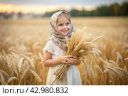 Russian Russian girl in a white dress and a Russian shawl holds golden ears of wheat against the background of a ripening field. The concept of planting and harvesting a rich harvest. Rural landscape. Стоковое AI-изображение, AI-художник Photojuli / Фотобанк Лори