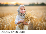 Russian Russian girl in a white dress and a Russian shawl holds golden ears of wheat against the background of a ripening field. The concept of planting and harvesting a rich harvest. Rural landscape. Стоковое AI-изображение, AI-художник Photojuli / Фотобанк Лори