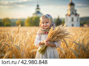Russian Russian girl in a white dress and a Russian headscarf holds golden ears of wheat against the background of a ripening field and an Orthodox church. The concept of planting and harvesting a rich harvest. Rural landscape. Стоковое AI-изображение, AI-художник Photojuli / Фотобанк Лори
