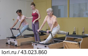 Svelte elderly woman performing set of pilates exercises on reformer during group workout. Active lifestyle and wellness concept of seniors. Стоковое видео, видеограф Яков Филимонов / Фотобанк Лори