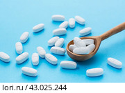 White oval pills in a wooden spoon on a blue background. Uncontrolled use of drugs in large quantities. Стоковое фото, фотограф Елена Руй / Фотобанк Лори