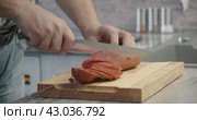 Man cuts thin slices of sausage on a wooden board with a knife. Close-up of the hands. Стоковое видео, видеограф EStarodubov / Фотобанк Лори
