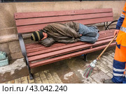 A homeless man sleeps on a bench on the street in the center of Moscow/ Бездомный бомж спит на лавке в центре Москвы, рядом с ним стоит дворник с метлой (2016 год). Редакционное фото, фотограф Iva Noel / Фотобанк Лори