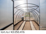 A new greenhouse made of polyethylene and polycarbonate with new beds made of Wood-polymer composite. Preparing for the spring garden season. Installation of a greenhouse in a suburban area. Стоковое фото, фотограф Photojuli / Фотобанк Лори