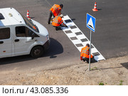ANGARSK, IRKUTSK REGION, RUSSIA - July 29, 2023: Top view of a team of road workers in orange vests marking a speed bump with white paint in the form of signal squares on sunny summer day. Редакционное фото, фотограф Виктория Катьянова / Фотобанк Лори