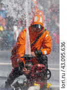 Fireman in an orange firefighter's protective uniform turns valve of fire hydrant giving stream of water spraying upward from fire hose (2019 год). Редакционное фото, фотограф А. А. Пирагис / Фотобанк Лори