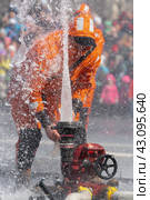 Firefighter Emercom of Russia in orange turnout gear turns valve of fire hydrant, causing jet of water to spray upwards from fire hose (2019 год). Редакционное фото, фотограф А. А. Пирагис / Фотобанк Лори