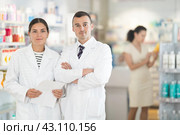 Positive man and girl pharmacists are standing in pharmacys sales hall, pharmacy staff are amicably preparing to meet chemist shop visitors. Стоковое фото, фотограф Яков Филимонов / Фотобанк Лори