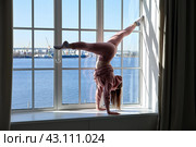 Handstand in front of window when young woman from cheerleader team trains at home under coronavirus quarantine. Стоковое фото, фотограф Владимир Григорьев / Фотобанк Лори