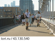 Moscow, Russia - July 24, 2022: People on street in summer day. Somebody rides renting motor scooter, other just walkd on foot. Every day life. Active lifestyle. Front  view. Street photography. Редакционное фото, фотограф YuryKara / Фотобанк Лори