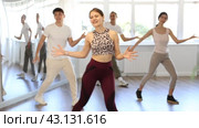 Smiling active young girl enjoying contemporary vigorous dance at group class in light mirrored studio. Стоковое видео, видеограф Яков Филимонов / Фотобанк Лори