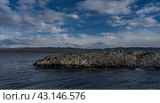 Many cormorants have settled on a rocky island in the Beagle Channel. Ripples on the blue ocean water. Clouds in the azure sky. Mountains in the distance. Argentina. Tierra del Fuego Archipelago. Стоковое фото, фотограф Вера Ивановна Кубарева / Фотобанк Лори