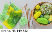 Video of wicker basket with balls and skeins of green and yellow wool yarn, knitting needles and striped handmade knitted fabric. Hand knitting square pattern using 10-stitch method. Flat lay, close-up. Стоковое видео, видеограф Виктория Катьянова / Фотобанк Лори