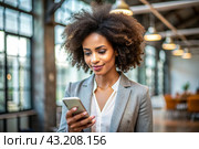 A businesslike dark-skinned African-American woman with curly hair. She is dressed in a casual jacket. In the hands of a smartphone. A businesswoman looks at her mobile phone. Стоковое AI-изображение, AI-художник Photojuli / Фотобанк Лори
