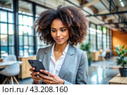 A businesslike dark-skinned African-American woman with curly hair. She is dressed in a casual jacket. In the hands of a smartphone. A businesswoman looks at her mobile phone. Стоковое AI-изображение, AI-художник Photojuli / Фотобанк Лори