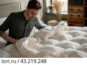 Young man smoothing out comforter on bed. Стоковое AI-изображение, AI-художник Иван Рябоконь / Фотобанк Лори