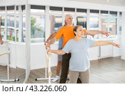 Mature woman in sportswear participating 2nd position of ballet stance at barre with group in choreography studio. Стоковое фото, фотограф Яков Филимонов / Фотобанк Лори