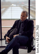 Train Station. Mature man in business clothes is sleeping, sitting in waiting room and waiting for train. Evening is dark. Стоковое фото, фотограф Natalia Gdovskaia / Фотобанк Лори