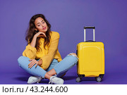 A thoughtful traveler girl sitting next to her luggage on a uniform lilac background. Copy space. The concept of vacation. Стоковое AI-изображение, AI-художник Ярославский Максим / Фотобанк Лори