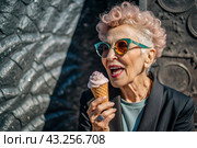 Portrait of an extraordinary, stylish, fashionable elderly woman, a pensioner of 70 years old, with ice cream in her hands on a city street. The concept of happy seniors and delicious desserts. Стоковое AI-изображение, AI-художник Photojuli / Фотобанк Лори