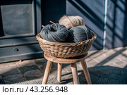 Balls of yarn in a wicker basket on a wooden stool. Needlework, textiles, knitting. Winter season, small business, handmade clothes. Стоковое AI-изображение, AI-художник Photojuli / Фотобанк Лори