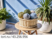 Balls of yarn in a wicker basket on a wooden stool. Needlework, textiles, knitting. Winter season, small business, handmade clothes. Стоковое AI-изображение, AI-художник Photojuli / Фотобанк Лори