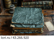 Image of antique books and ancient manuscripts on a wooden table. Old leather-bound books and yellowed manuscript pages create an atmosphere of the past and history. A neatly folded stack of manuscripts with elegant ink inscriptions on darkened paper attracts attention. The background is filled with books with vintage spines, adding depth and detail to the composition. This image is ideal for use in projects related to history, literature, antiques and vintage style. Стоковое AI-изображение, AI-художник Анна Кривицкая / Фотобанк Лори